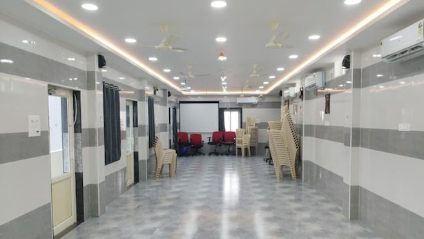 A hotel lobby with a marble floor, ceiling fans, a projection screen, and rows of chairs. - BK Stays (Chirala)