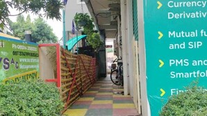 A staircase leading to a building with a green sign listing services like Equity, Currency Derivative, Mutual Funds, and Smartfool. - BK Stays (Chirala)