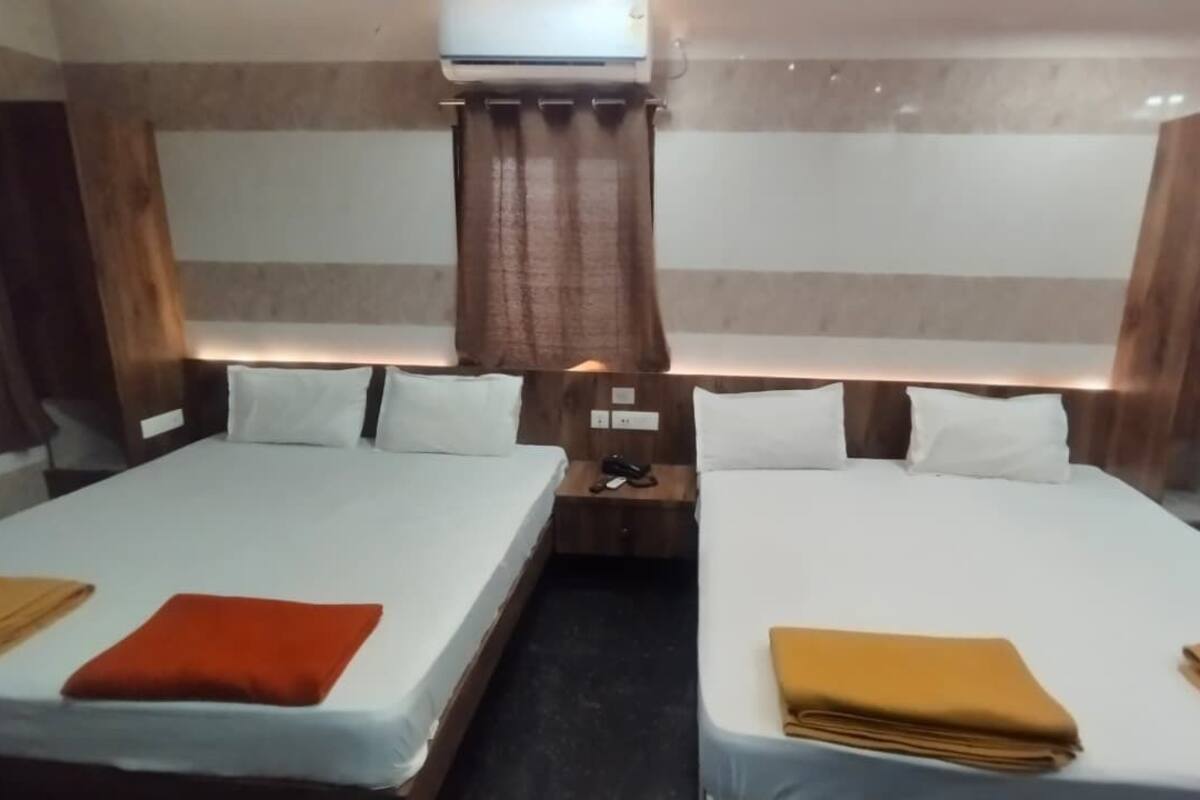 A hotel room with two beds, a nightstand, and an air conditioning unit.