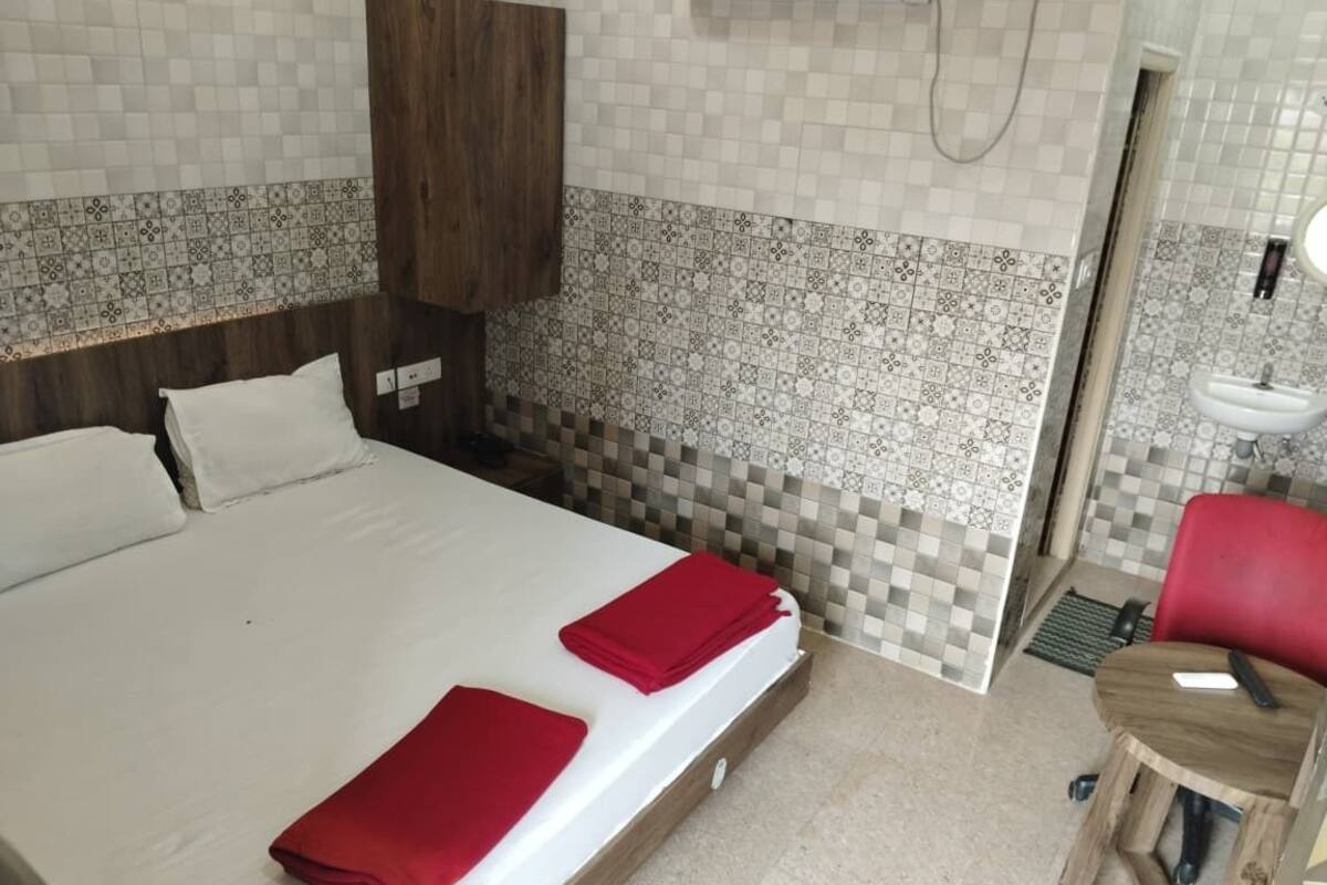 A hotel room with a large bed, two red towels, a wooden headboard, a wooden cabinet, a tiled wall, and a small wooden table with a remote control.