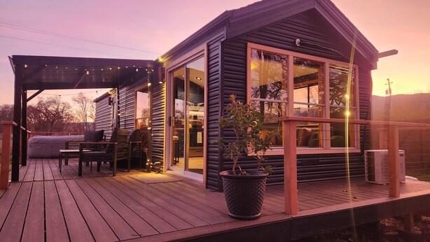Une cabane chaleureuse avec une terrasse en bois, de grandes fenêtres et un patio couvert.
