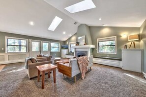 A spacious living room with a fireplace, large windows, and a high ceiling with skylights. - New Listing! Bright and Open, Minnow's Run (Kings Beach)