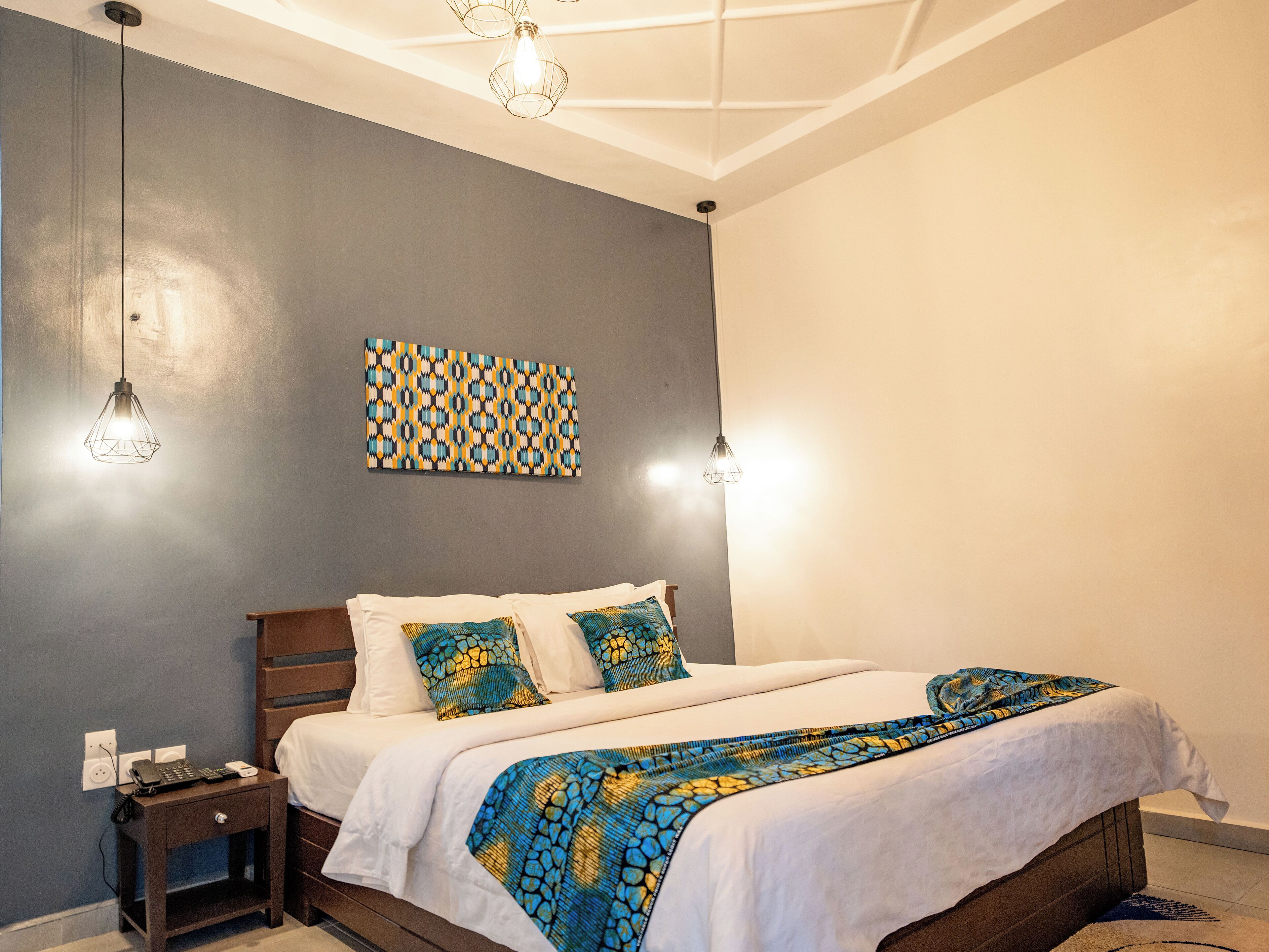 A bedroom with a bed, bedside tables, a wall-mounted artwork, and pendant lights.