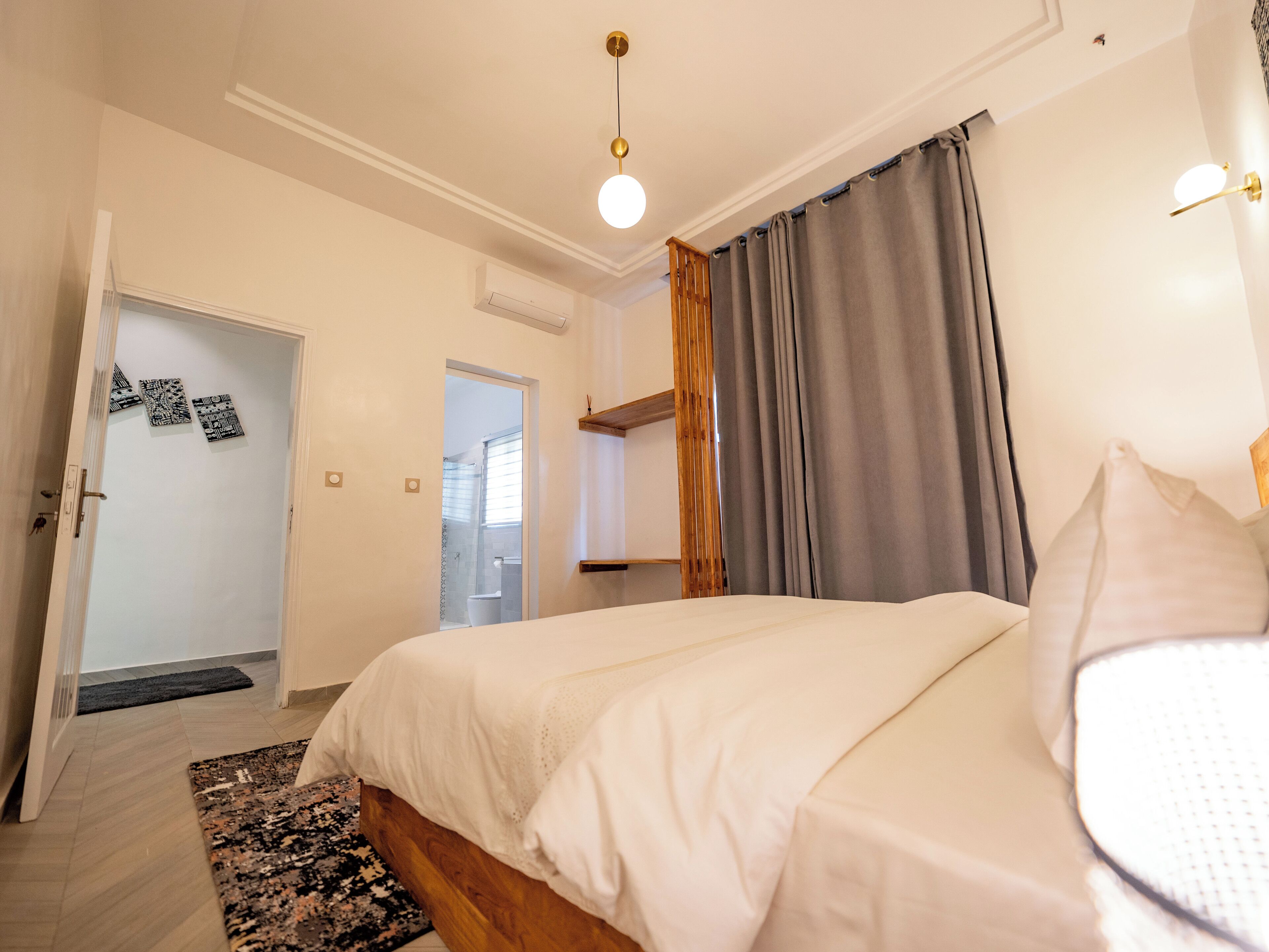 Ein Schlafzimmer mit Bett, einer Tür, einer Wand-Klimaanlage und einem Fenster mit Vorhängen.
