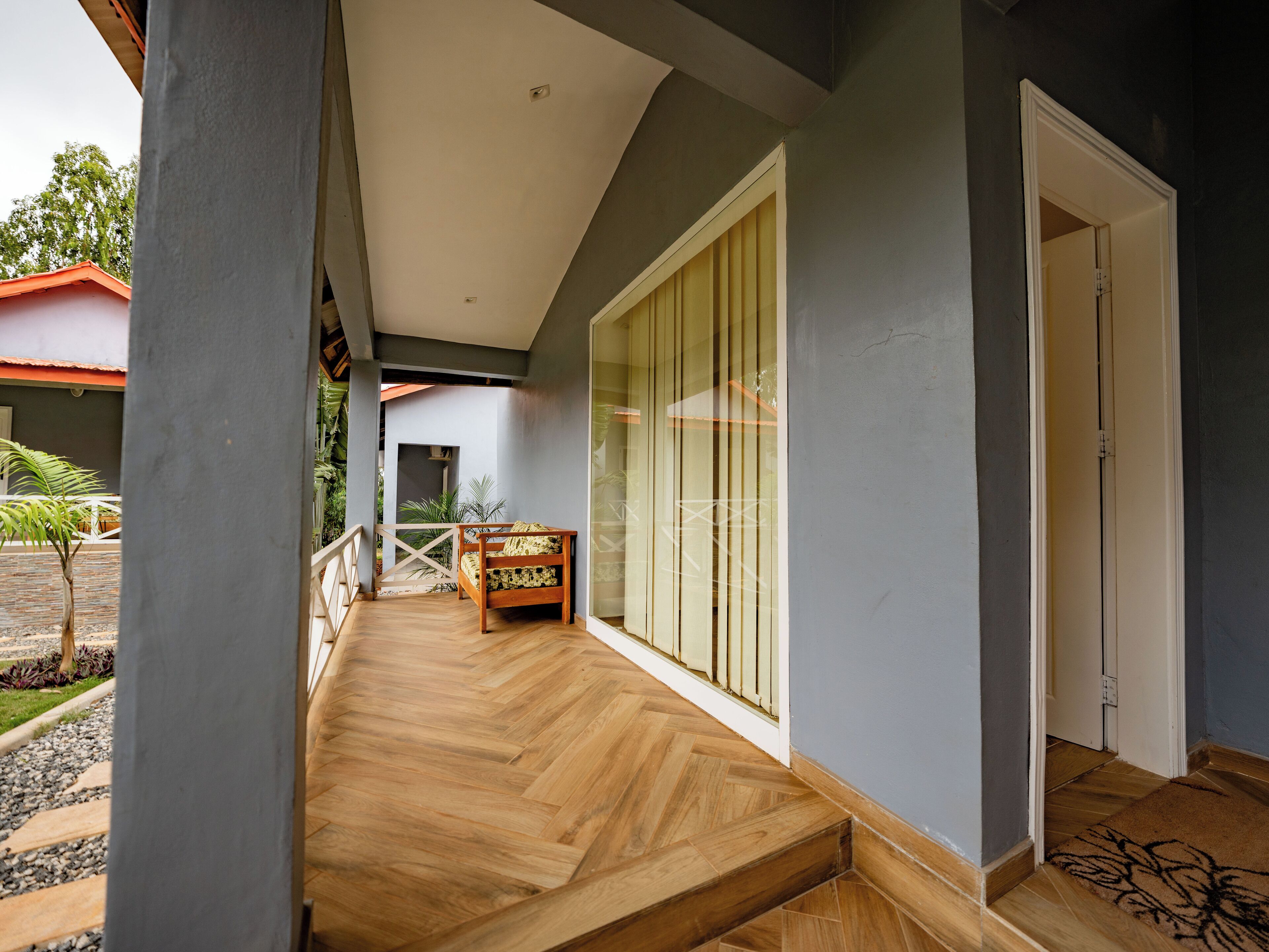 A wooden deck with a bench, a glass door, and a view of a building with a red roof.