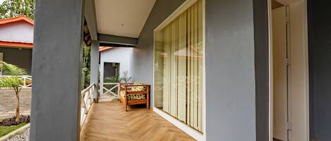 Una terraza de madera con un banco, un ventanal de vidrio y vista a un edificio de techo rojo.