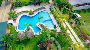 Une vue aérienne d’un complexe hôtelier doté d’une piscine entourée d’une végétation luxuriante, de palmiers et d’un espace abrité avec des sièges.