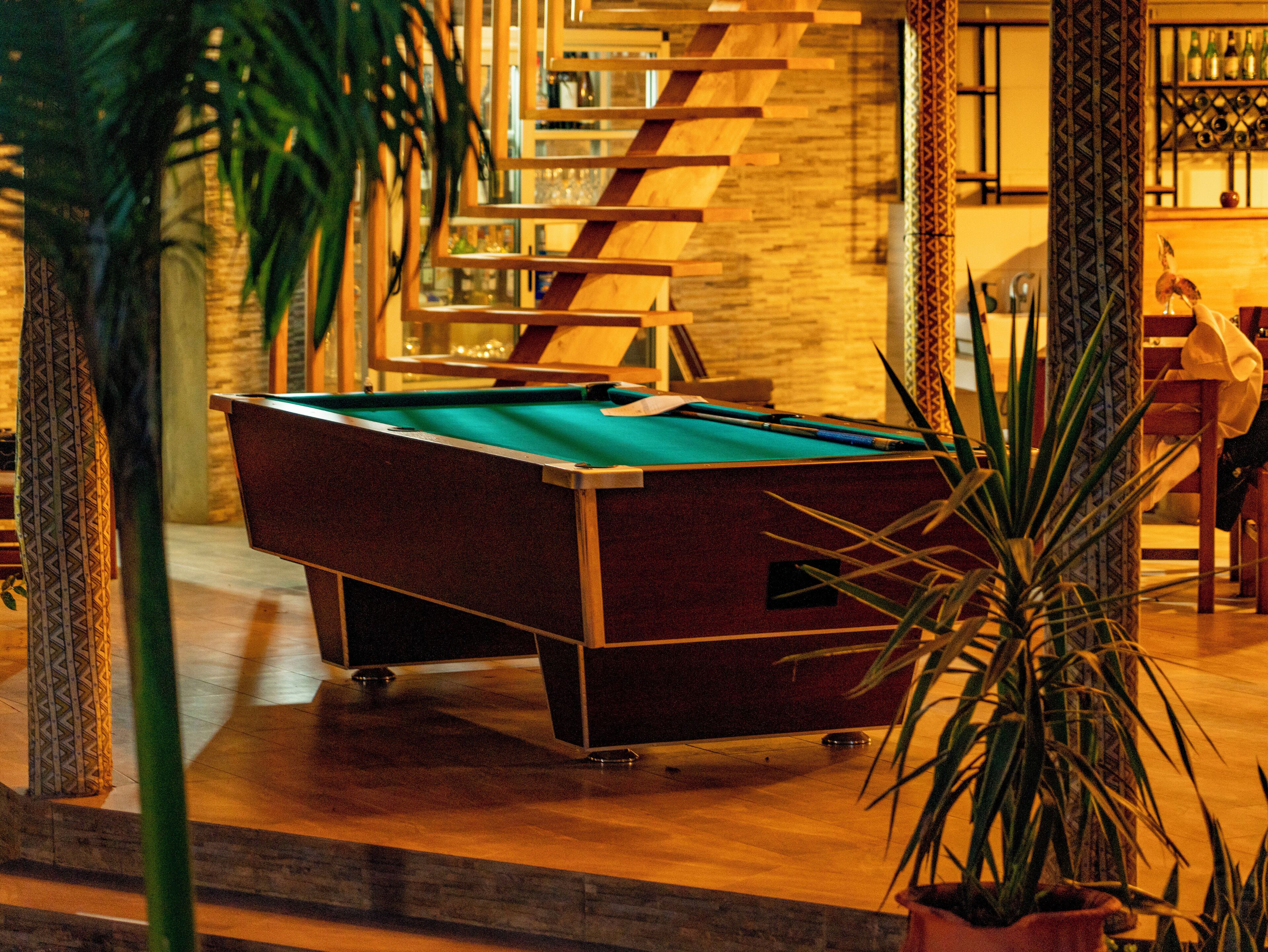 A pool table in a room with a wooden floor and a staircase in the background.