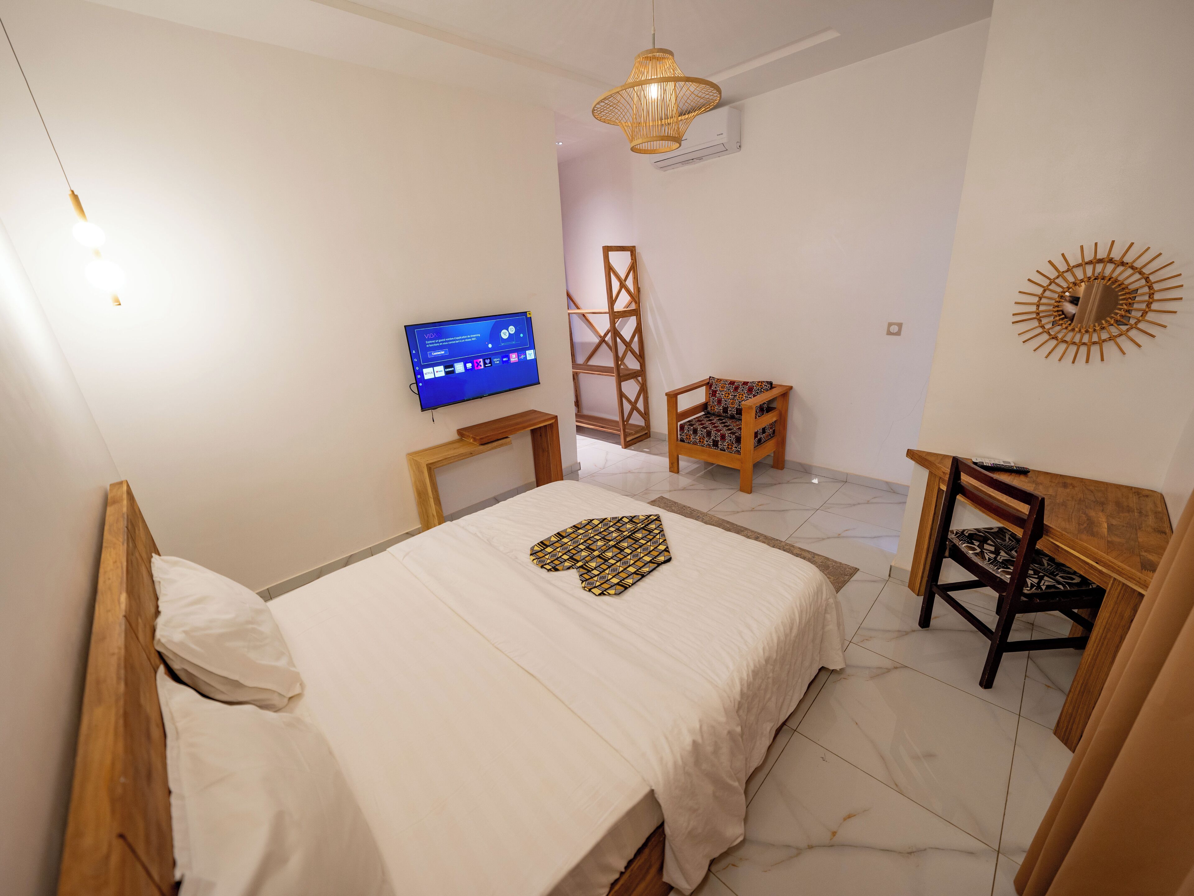 A bedroom with a bed, a TV, a wooden chair, a wooden desk, and a decorative wall piece.
