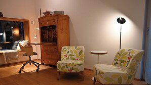 A cozy room with a wooden floor, a desk with a chair, a small round table, and two patterned armchairs. - Vacation home with all the amenities (air-conditioned/sauna) (Sternenfels)