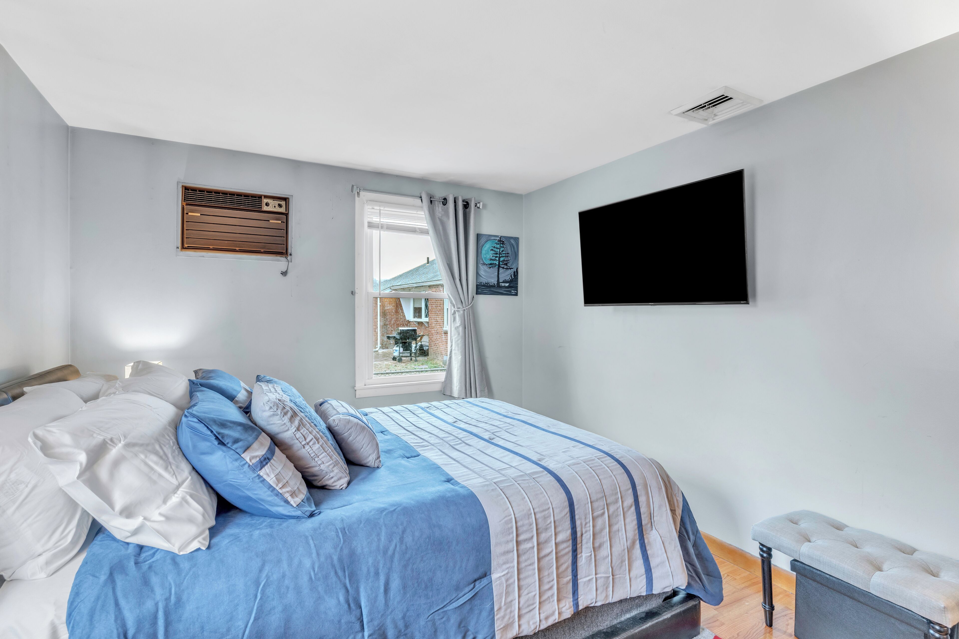 A bedroom with a bed, a window with curtains, a mounted TV, and a wall-mounted heater.
