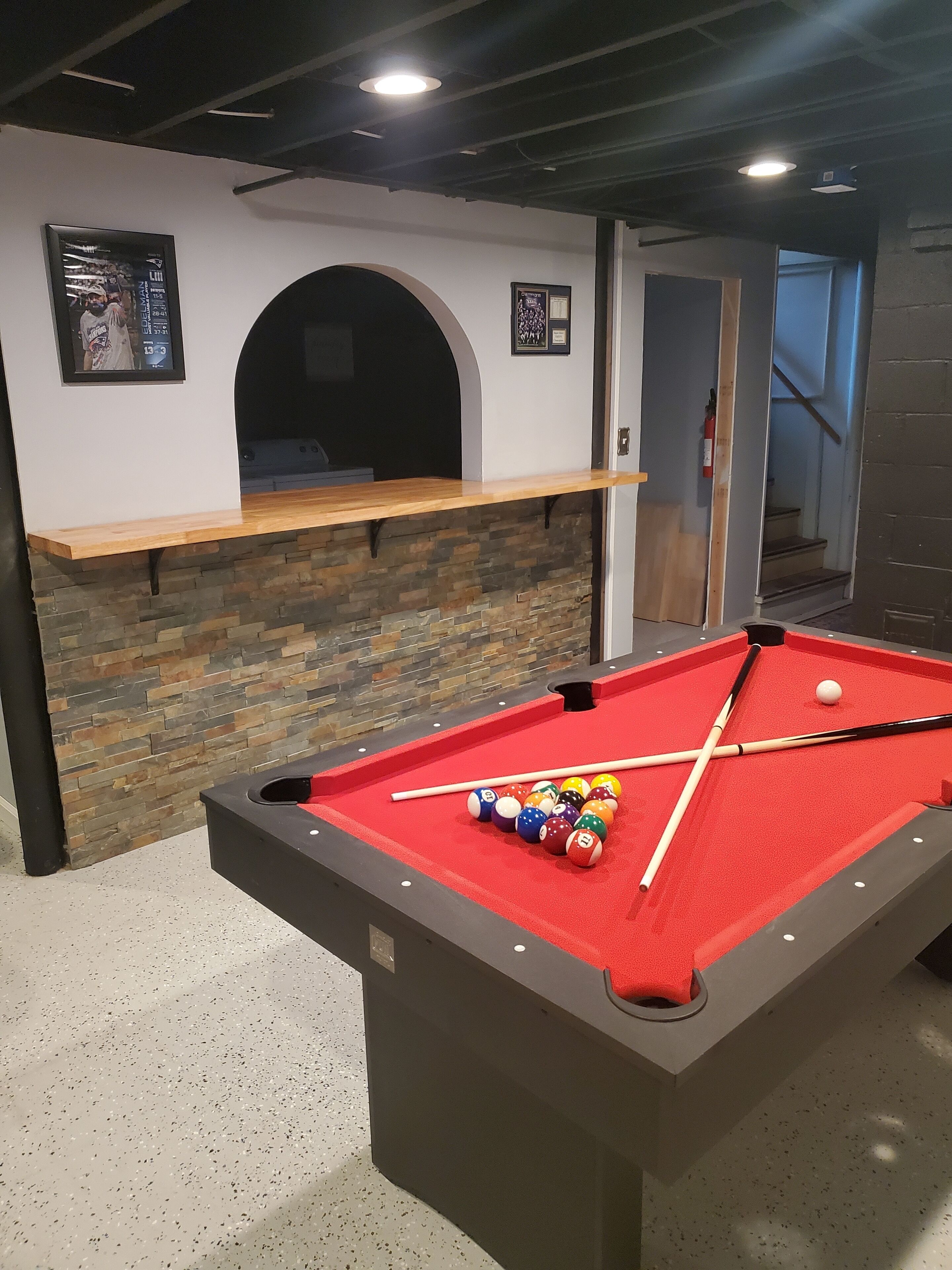 A pool table with balls and cues, a stone wall, and a shelf with framed pictures.