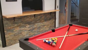 A pool table with balls and cues, a stone wall, and a shelf with framed pictures.