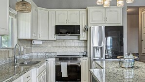 Una cocina con armarios blancos, un refrigerador de acero inoxidable, horno empotrado y encimera de granito.
