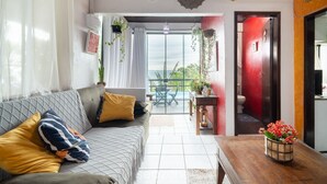 A living room with a sofa, a wooden table, and a balcony with a view. - House w/ Ocean View, Pool and Beach Access Ize0016 (Florianópolis)