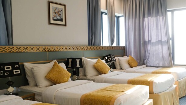 A hotel room with four beds, each with a yellow bedspread and white pillows. There is a framed picture on the wall above the beds, and a window with curtains. - Saraya Abeer Hotel Company (Makkah)