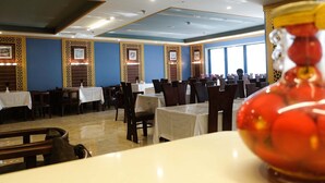 A restaurant with tables and chairs, framed pictures on the walls, and a large window. - Saraya Abeer Hotel Company (Makkah)