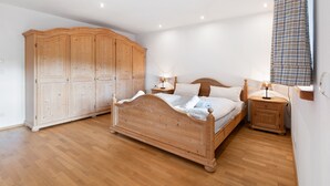 Une chambre à coucher avec un lit en bois, deux tables de chevet avec des lampes, une armoire et une grande fenêtre avec un rideau.
