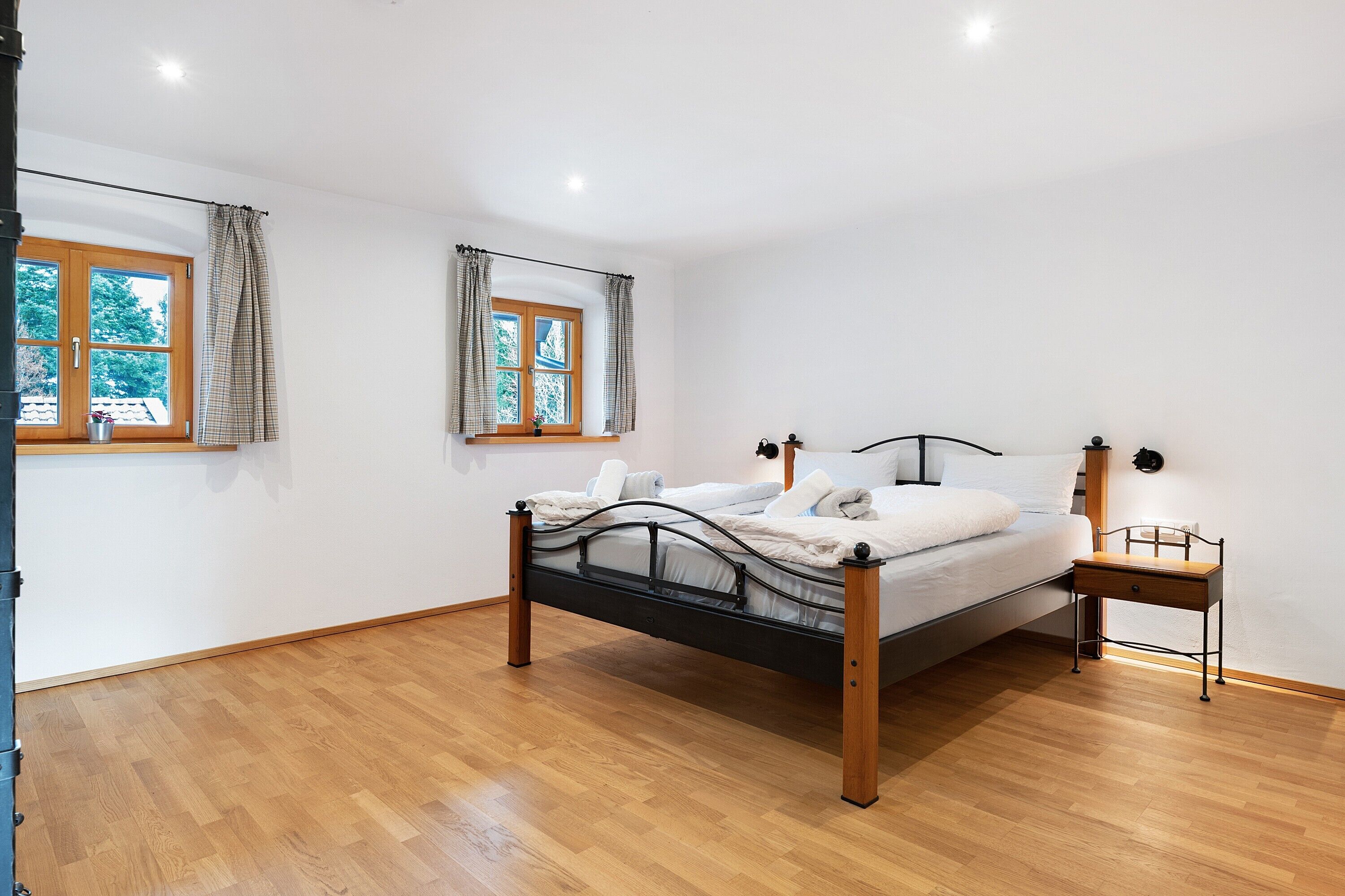 A bedroom with a bed, a nightstand, a window with curtains, and a wooden floor.