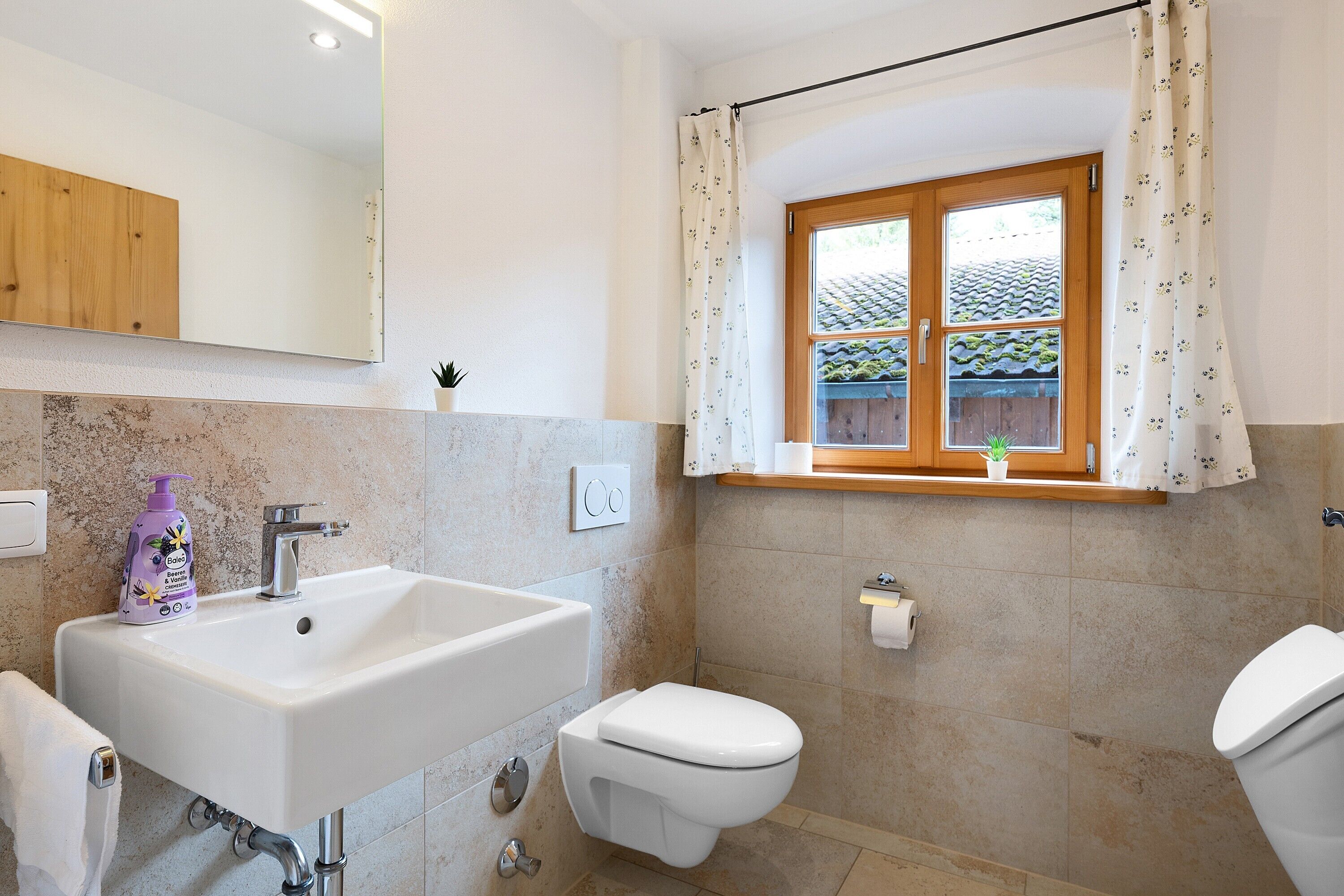 Een badkamer met een wastafel, toilet en raam met gordijnen.
