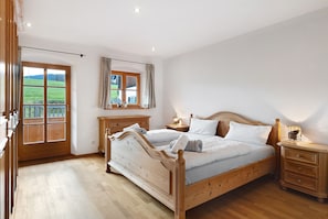 A bedroom with a wooden bed, bedside tables, a window with curtains, and a view of a green field.