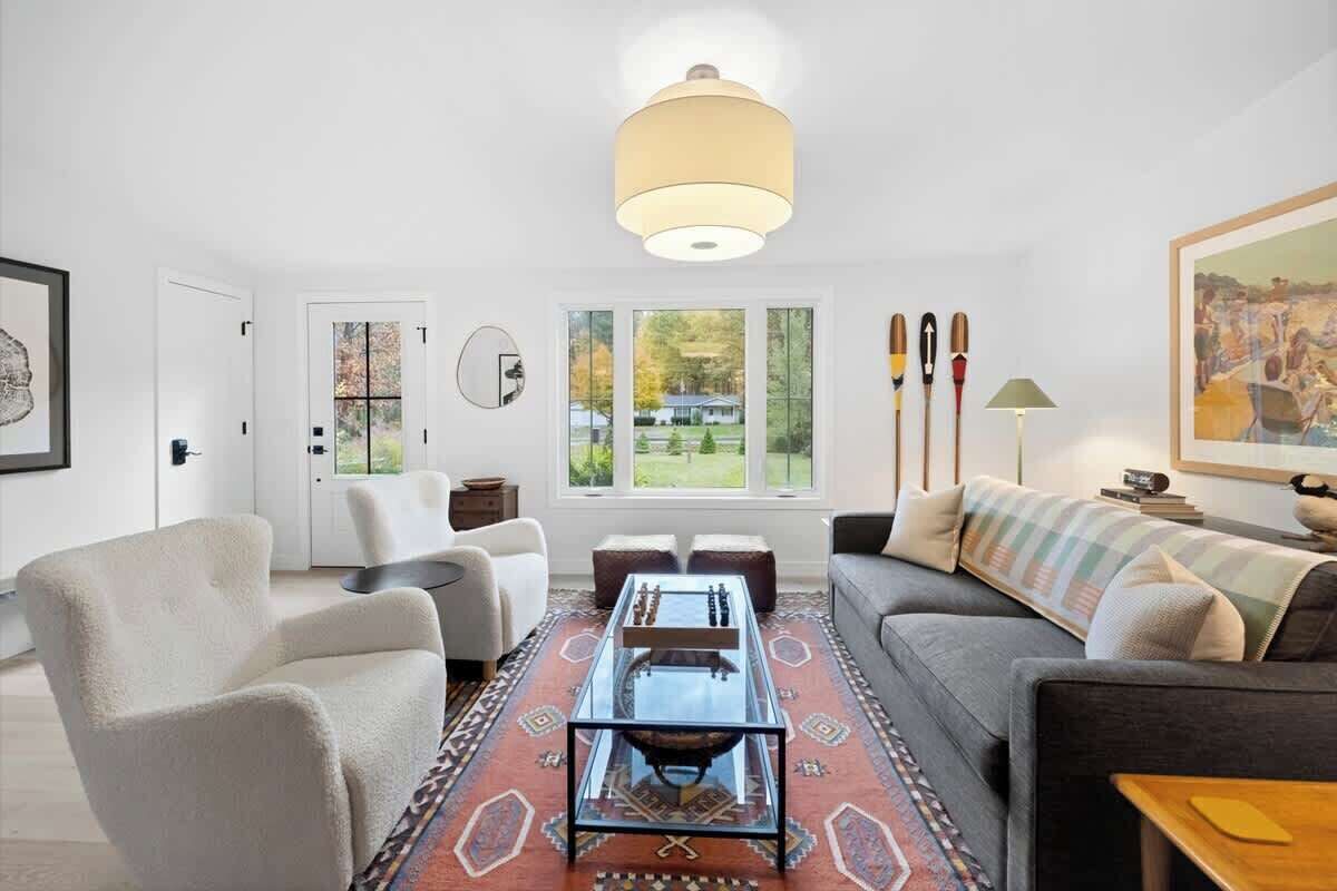 Ett vardagsrum med en soffa, fåtöljer, ett soffbord, en matta och en tavla.