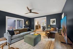 A modern living room with a grey sofa, wooden coffee table, and a ceiling fan. - Juniper Presents: Fennville Stay - Fire Pit near Saugatuck & Lake (Fennville)