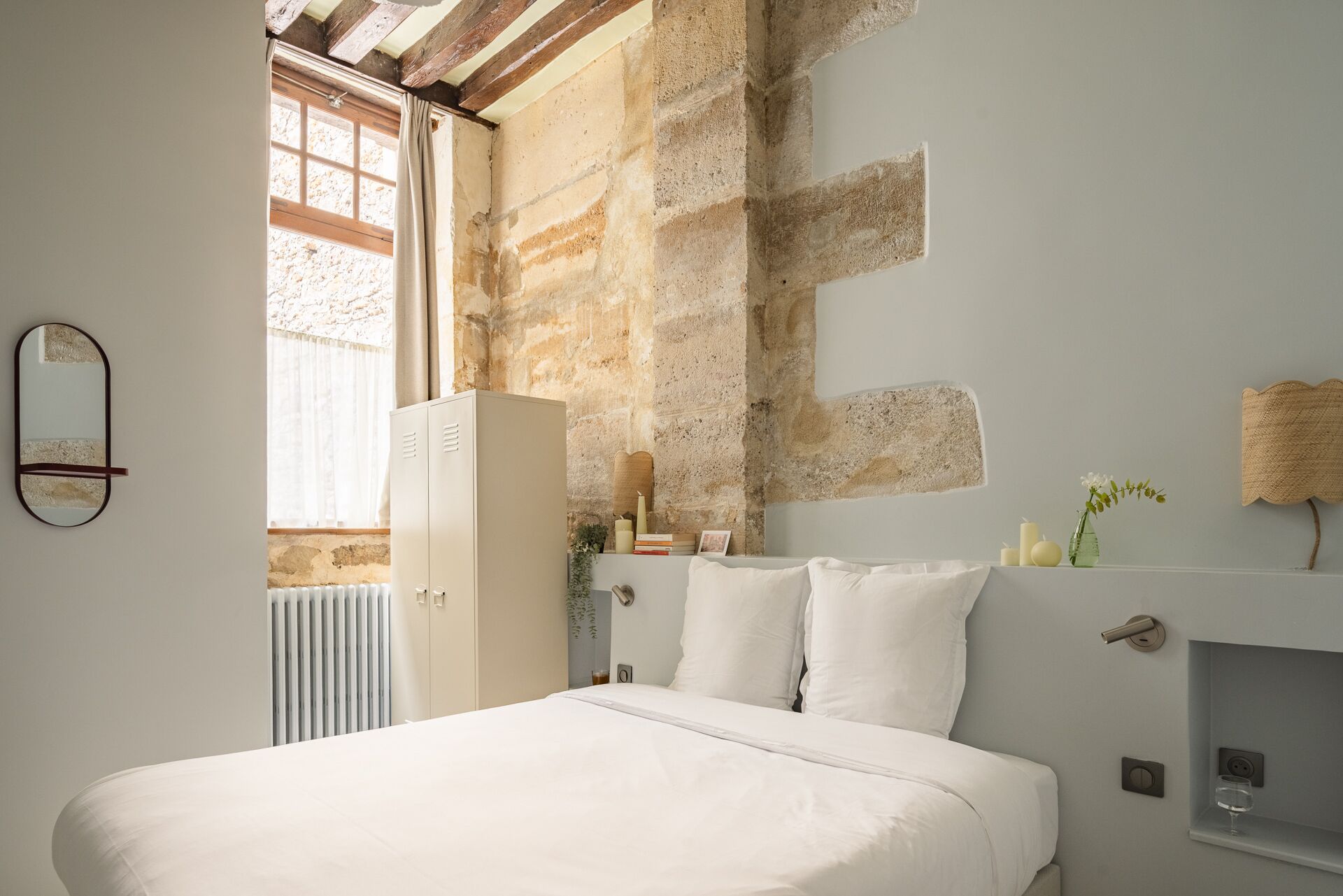 A bedroom with a large bed, a wardrobe, a mirror, and a stone wall.