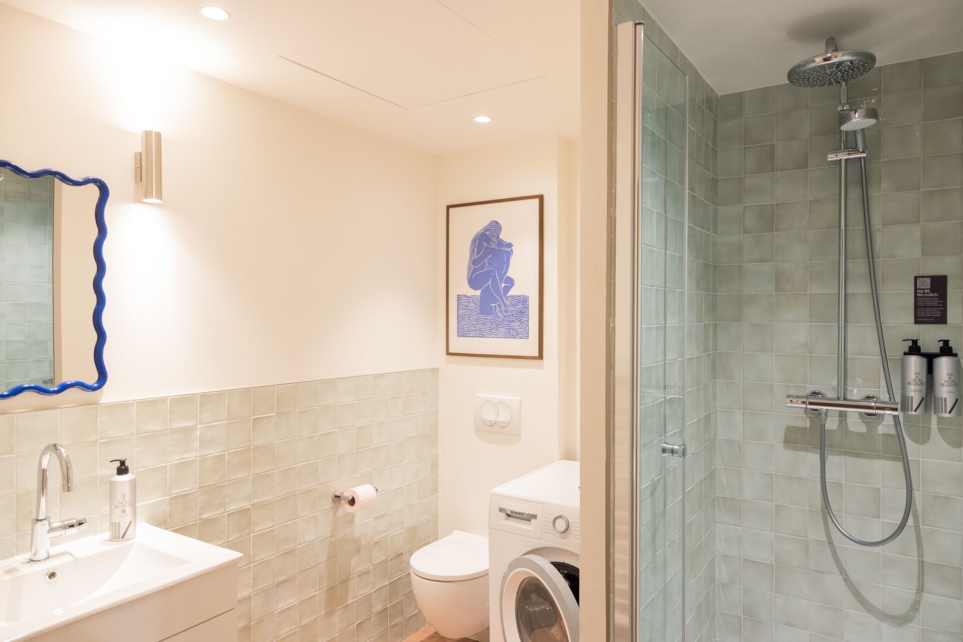 A bathroom with a sink, toilet, washing machine, and glass-enclosed shower.