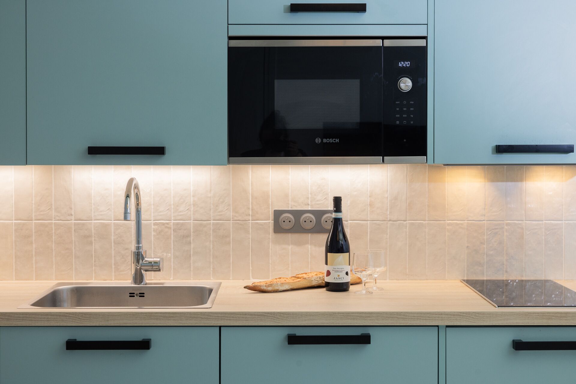 A kitchen with a Bosch microwave, a sink, and a wine bottle.