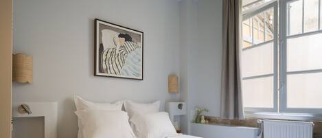 Une chambre à coucher avec un lit, un tableau, une fenêtre et un radiateur.