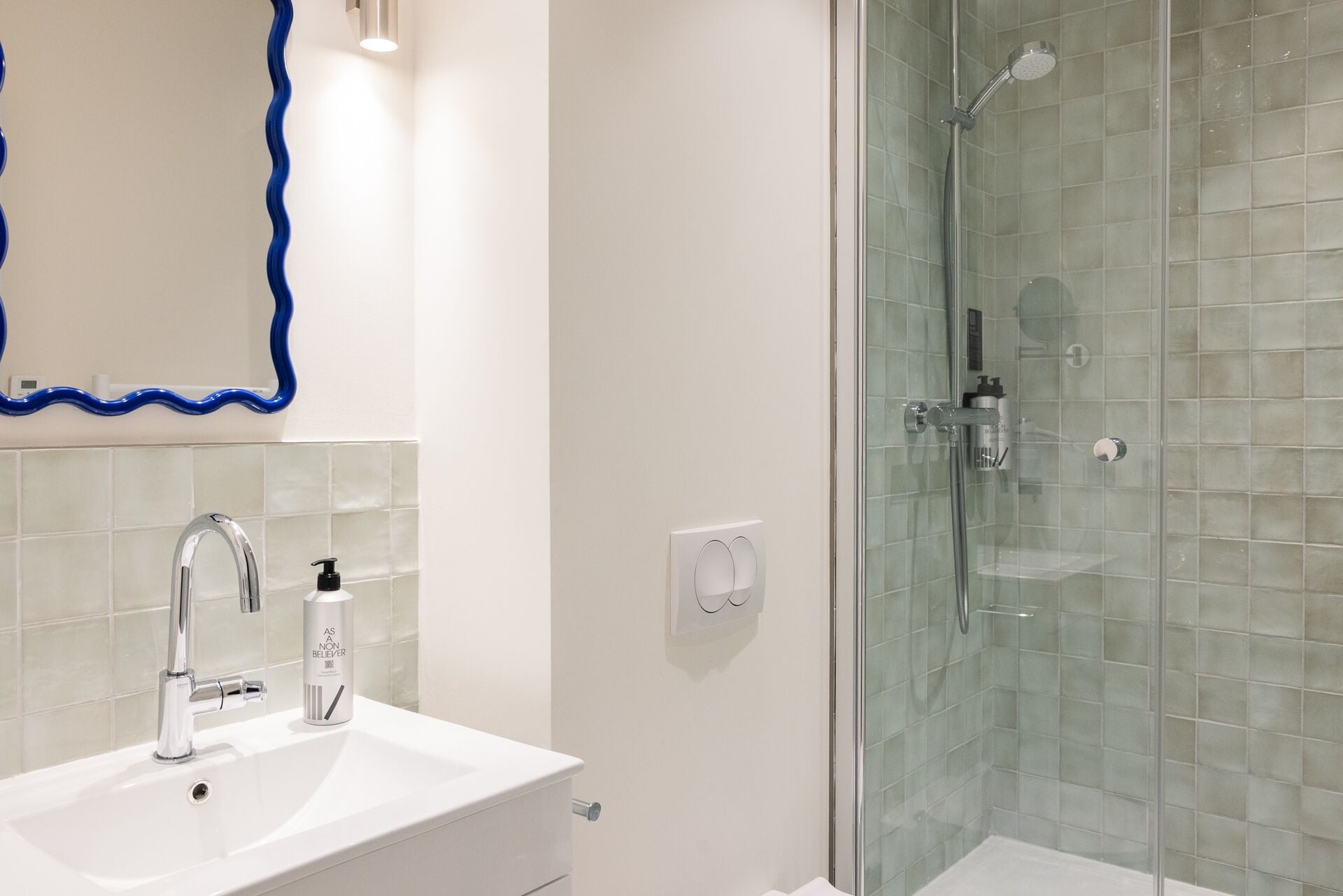 Ein Badezimmer mit einem weißen Waschbecken, einem Spiegel mit blauem Rahmen, einer Glasdusche und einer weiß gefliesten Wand.
