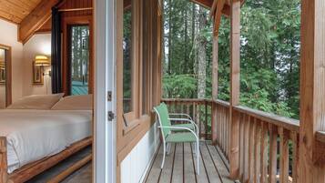 Une terrasse en bois avec un lit et une chaise, donnant sur une zone boisée.