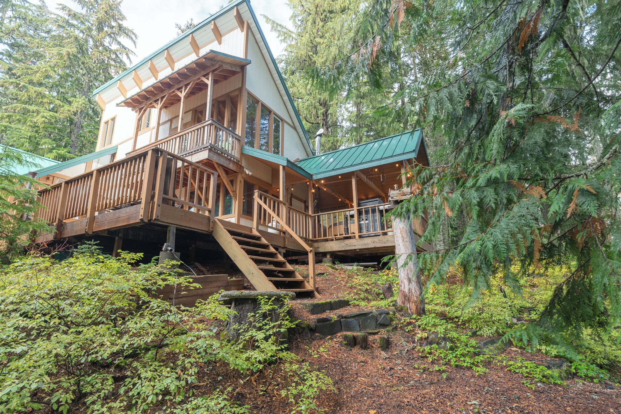 Une cabane dotée d’une terrasse en bois, d’un escalier et offrant une vue sur les arbres environnants.