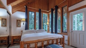 A wooden-framed bed with a bench, two bedside tables, and a door with a view of trees. - Third night free on stays before 8/30/26 (Government Camp)