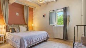 A bedroom with a bed, a window with curtains, a bedside table with a lamp, and a radiator.