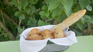 A basket of croissants and a baguette on a table with a green background.