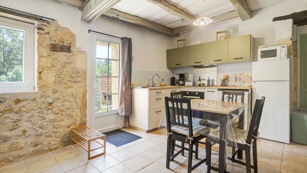 A kitchen with stone walls, wooden beams, a dining table with chairs, and a refrigerator.