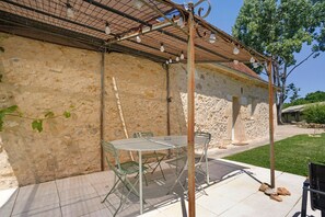 Un bâtiment en pierre doté d’une pergola, d’une table et de chaises d’extérieur, ainsi que d’une zone herbeuse.