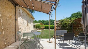 A patio area with a table and chairs, a pergola with lights, and a stone wall.