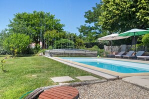 Una piscina con cubierta de madera, sillas de descanso y una sombrilla.