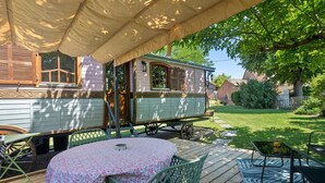 Eine überdachte Terrasse mit Tisch und Stühlen, ein Vintage-Wohnwagen und ein Rasenstück.