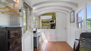 Ein Zimmer mit Holzboden, einem Schminktisch, einem Bett, einem Fenster und einer Küchenzeile mit Schränken und einer Mikrowelle.