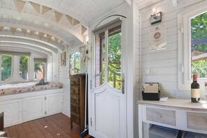 Una habitación con techo curvo, un banco con cojines, un aparador de madera, una puerta con ventanal y una encimera con una botella y papeles.