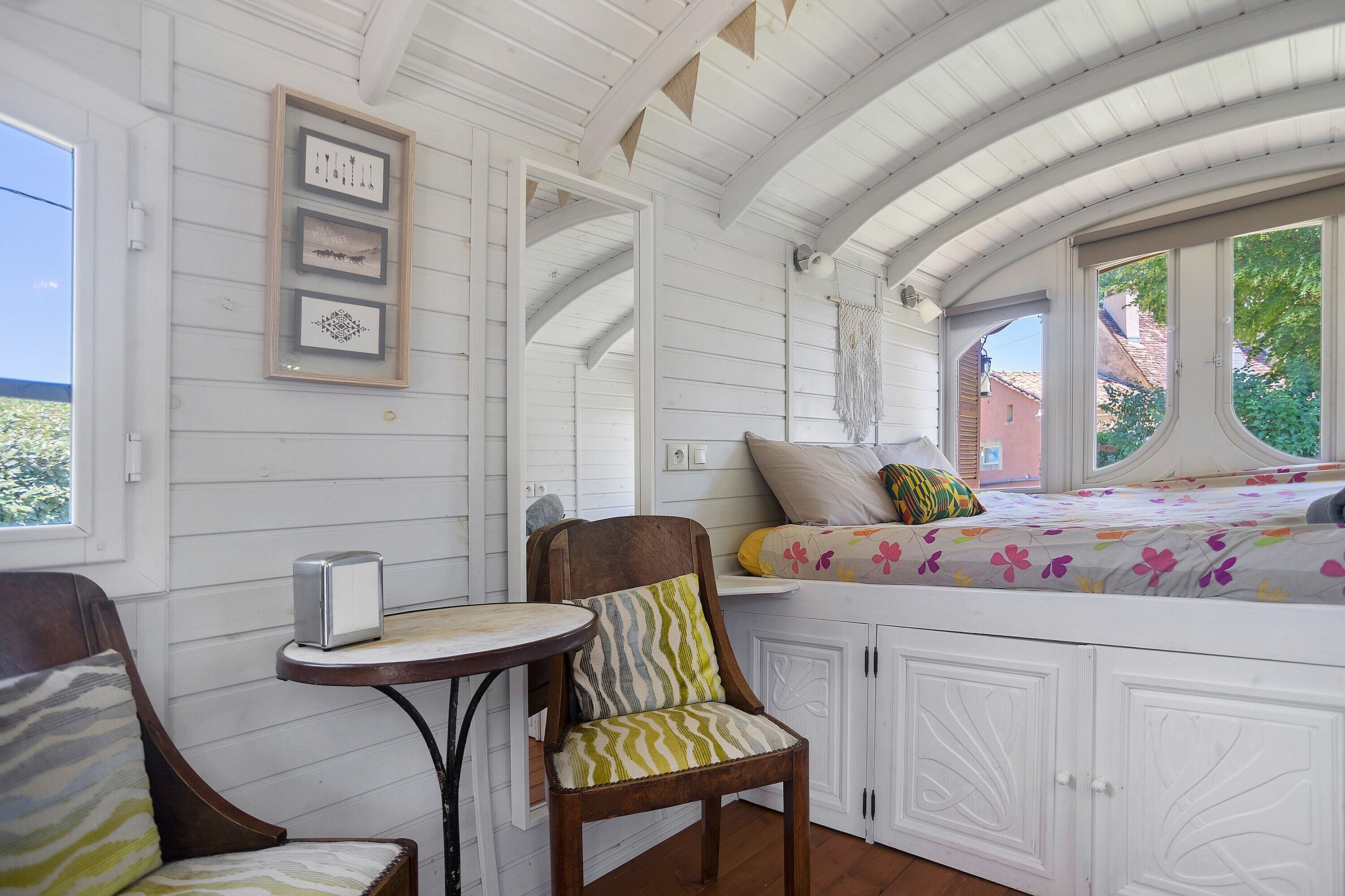 A cozy room with a bed, a chair, a small table, and framed artwork on the wall.