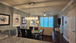 A dining area with a glass table and chairs, a ceiling fan, and artwork on the walls. - Emerald Isle 1301 - New listing! Front row beach chairs included! (Panama City Beach)