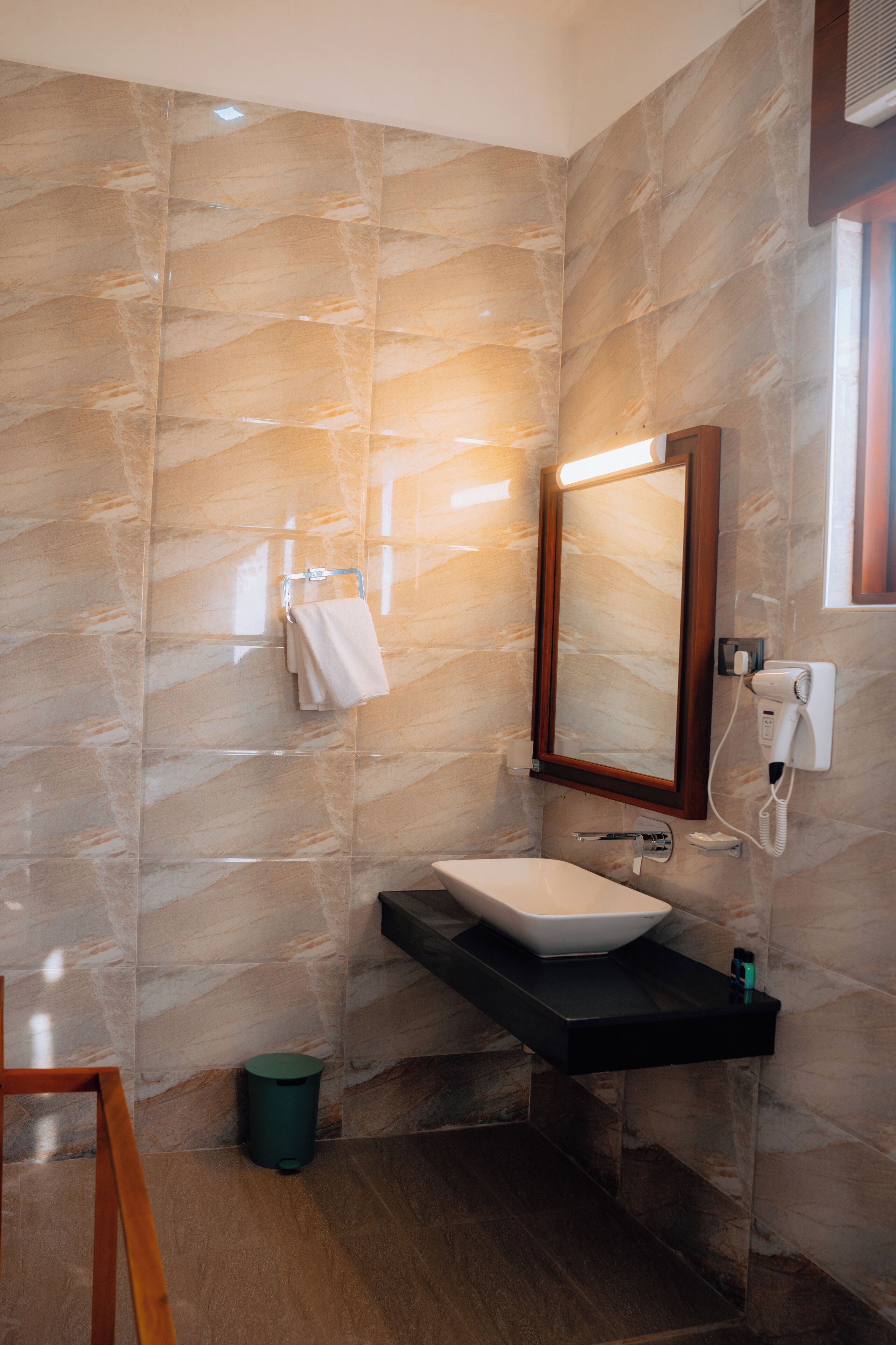 Un baño moderno con pared de mármol, un lavamanos blanco, un espejo y un secador de pelo.