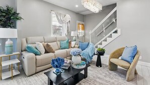 Una sala de estar moderna con un sofá color beige, una mesa de centro negra y una escalera al fondo.