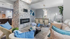 Una sala de estar moderna con chimenea de piedra, un comedor con candelabro y una zona de estar con cojines azules.