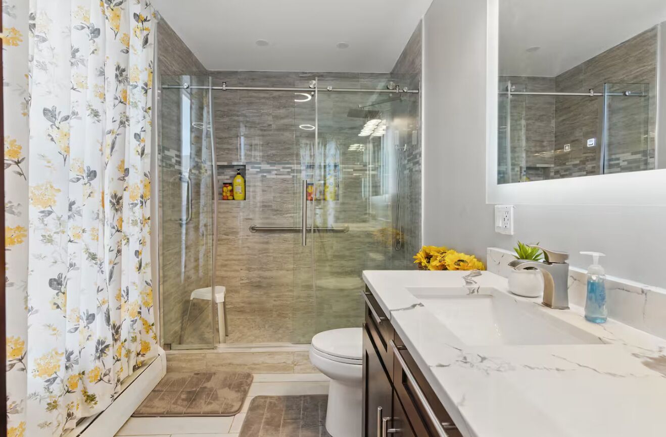 A modern bathroom with a glass shower enclosure, a white sink, and a marble countertop.
